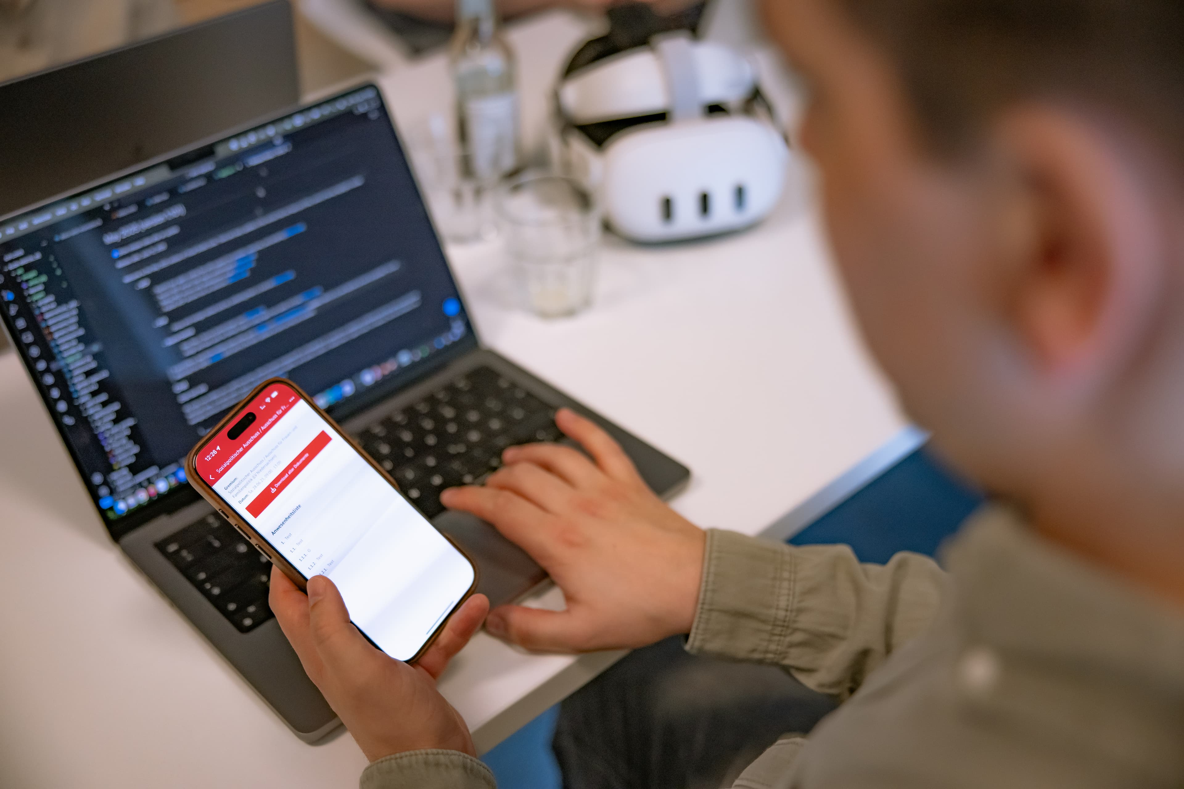 Christian hält Handy mit App und programmiert am Laptop